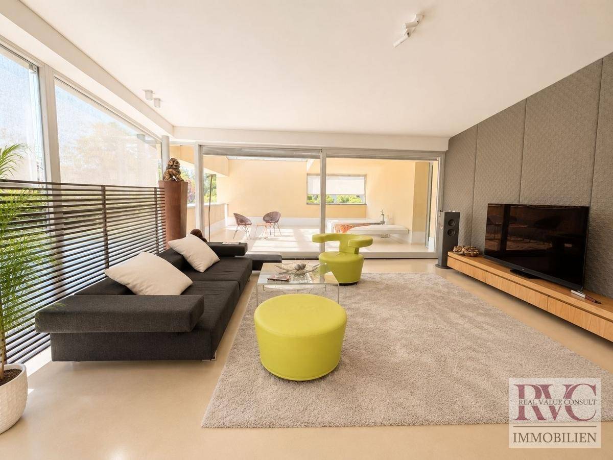 Modernes Wohnzimmer mit großen Fensterfronten, bequemer Couch und Zugang zur Terrasse.
