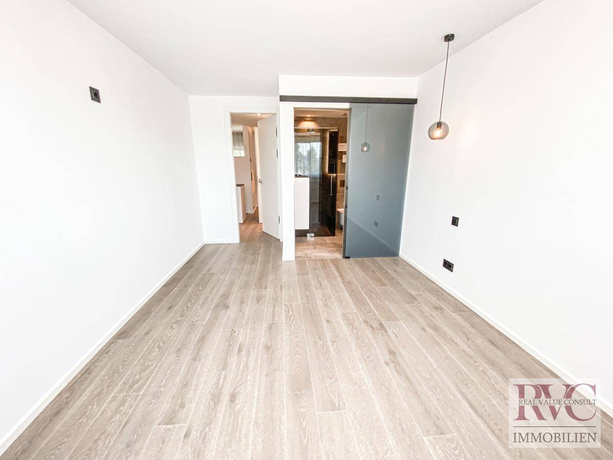 Helles Zimmer mit Holzboden und moderner Schiebetür zum angrenzenden Badezimmer.
