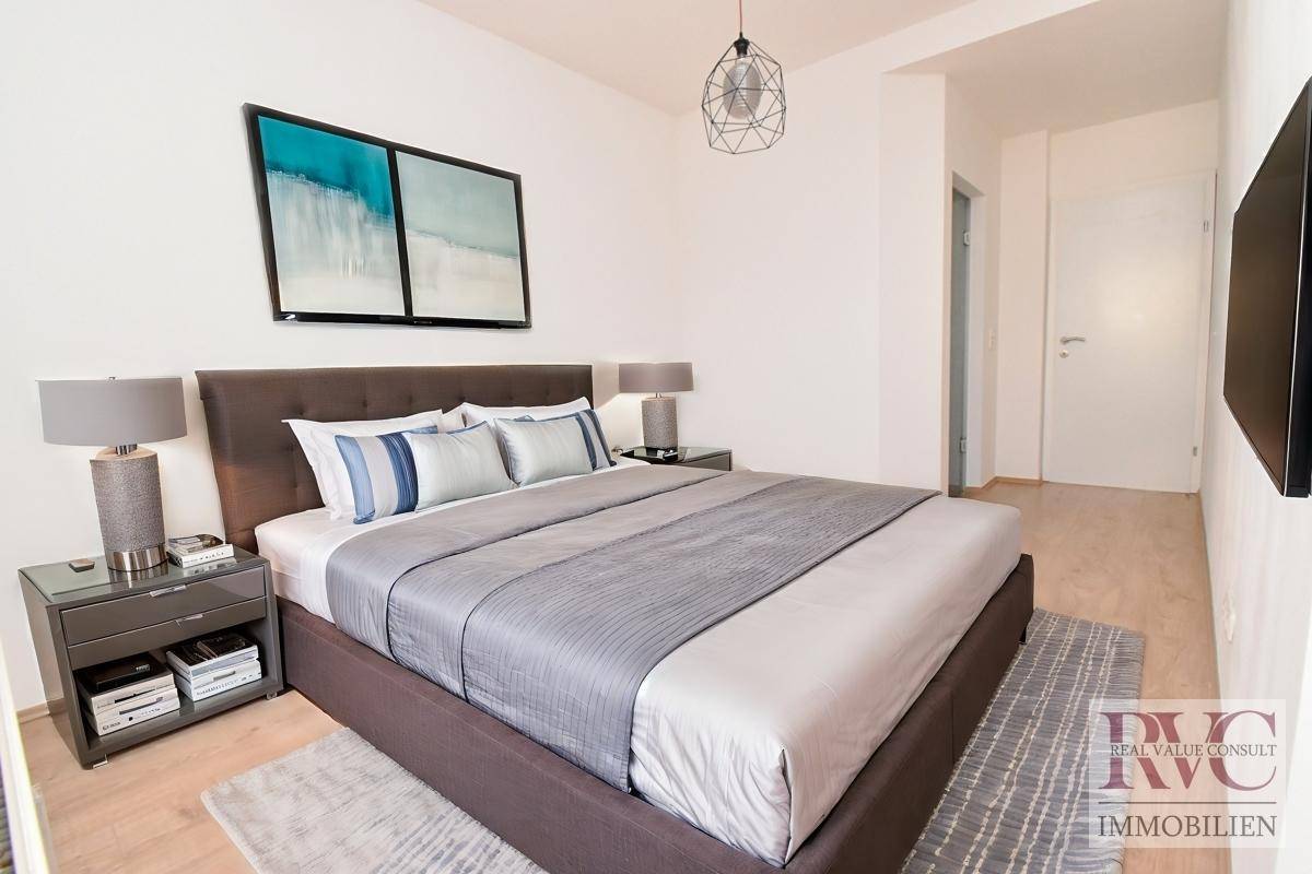 Modernes Schlafzimmer mit Doppelbett, Nachttischen und Wandfernseher in neutralen Farbtönen.