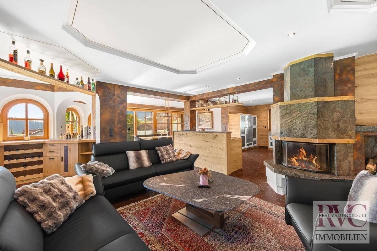 Gemütliches Wohnzimmer mit großem Kamin, bequemen Ledersofas und Blick auf den Barbereich.