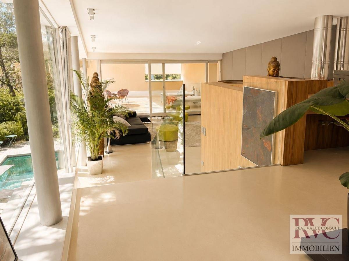 Heller, offener Wohnbereich mit großen Glasfronten, Blick auf den Pool und Zugang zur Terrasse.