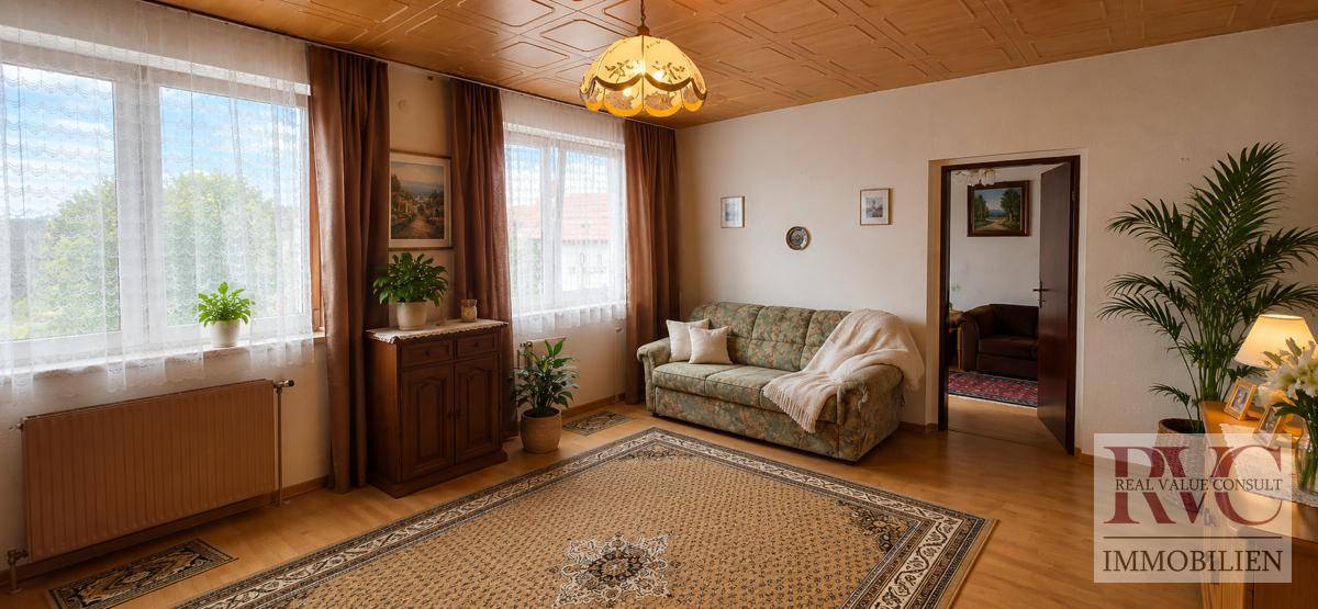 Helles Wohnzimmer mit gemütlichem Sofa, Holzboden und Blick ins Grüne durch große Fenster.