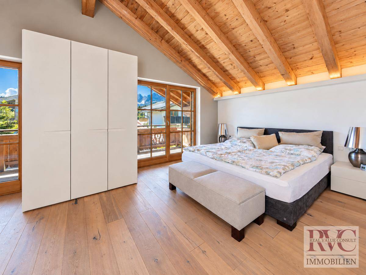 Helles Schlafzimmer mit Holzboden, Einbauschränken und Zugang zu einem Balkon.