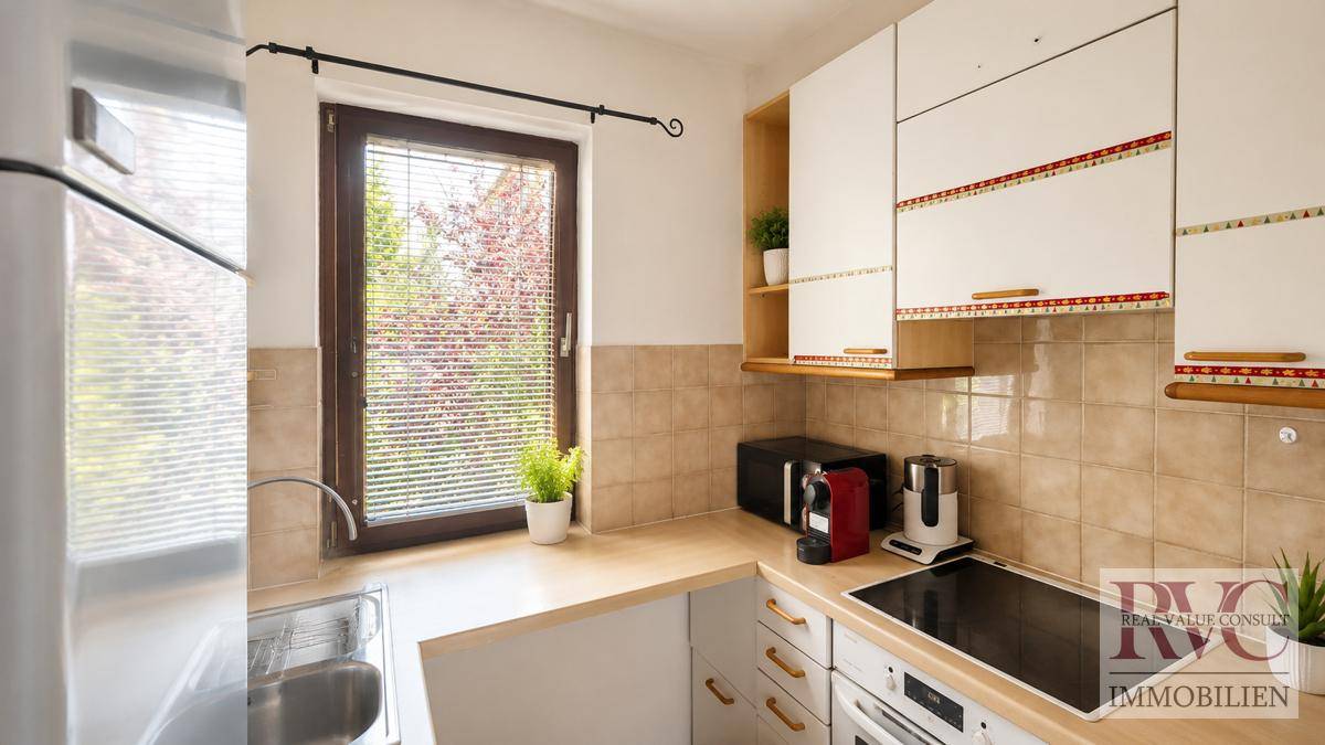 Funktionale Küche mit hellen Schränken, Holz-Arbeitsplatte und Fenster mit Blick ins Grüne.