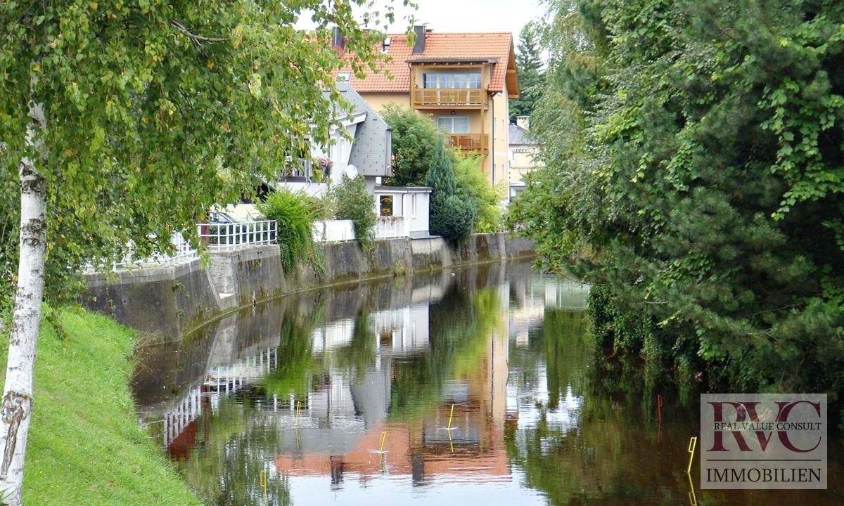 Idyllischer Kanal mit grünen Ufern und Spiegelungen der umliegenden Häuser.
