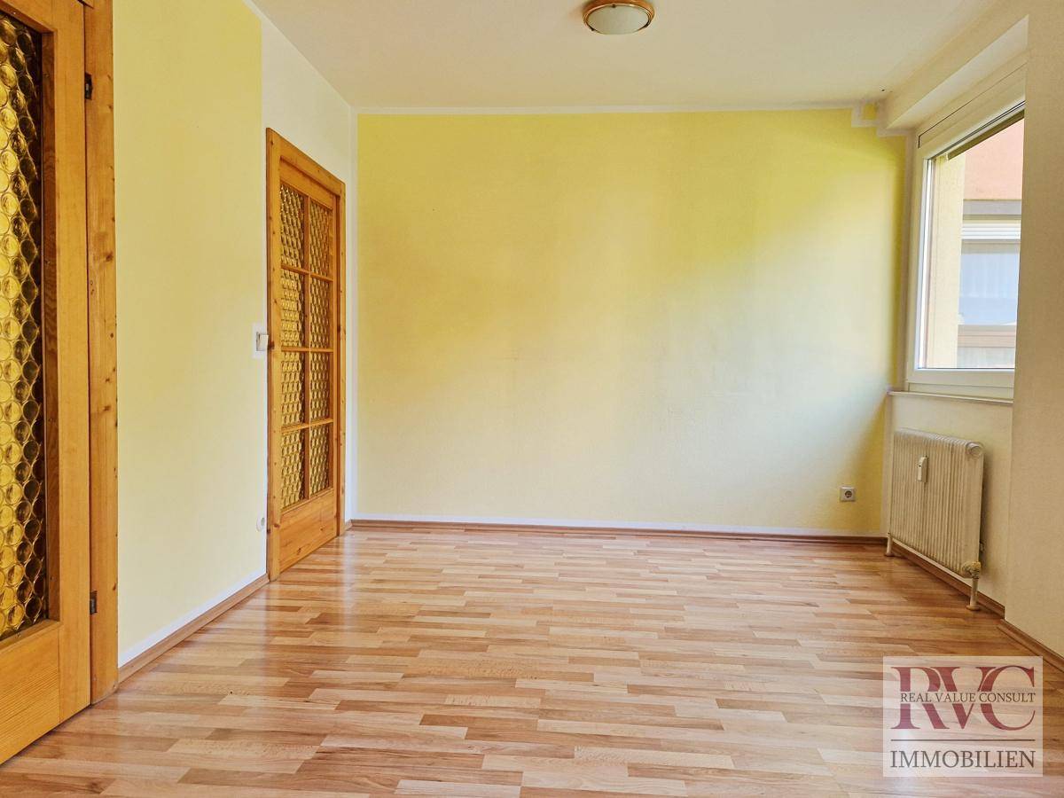 Helles Zimmer mit Parkettboden und gelber Akzentwand.