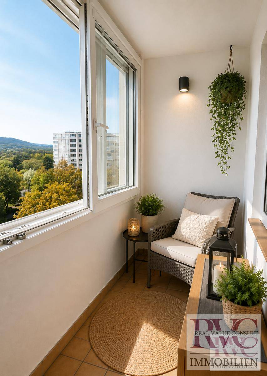 Kleiner, verglaster Balkon mit Sitzgelegenheit und Blick ins Grüne sowie auf die Umgebung.