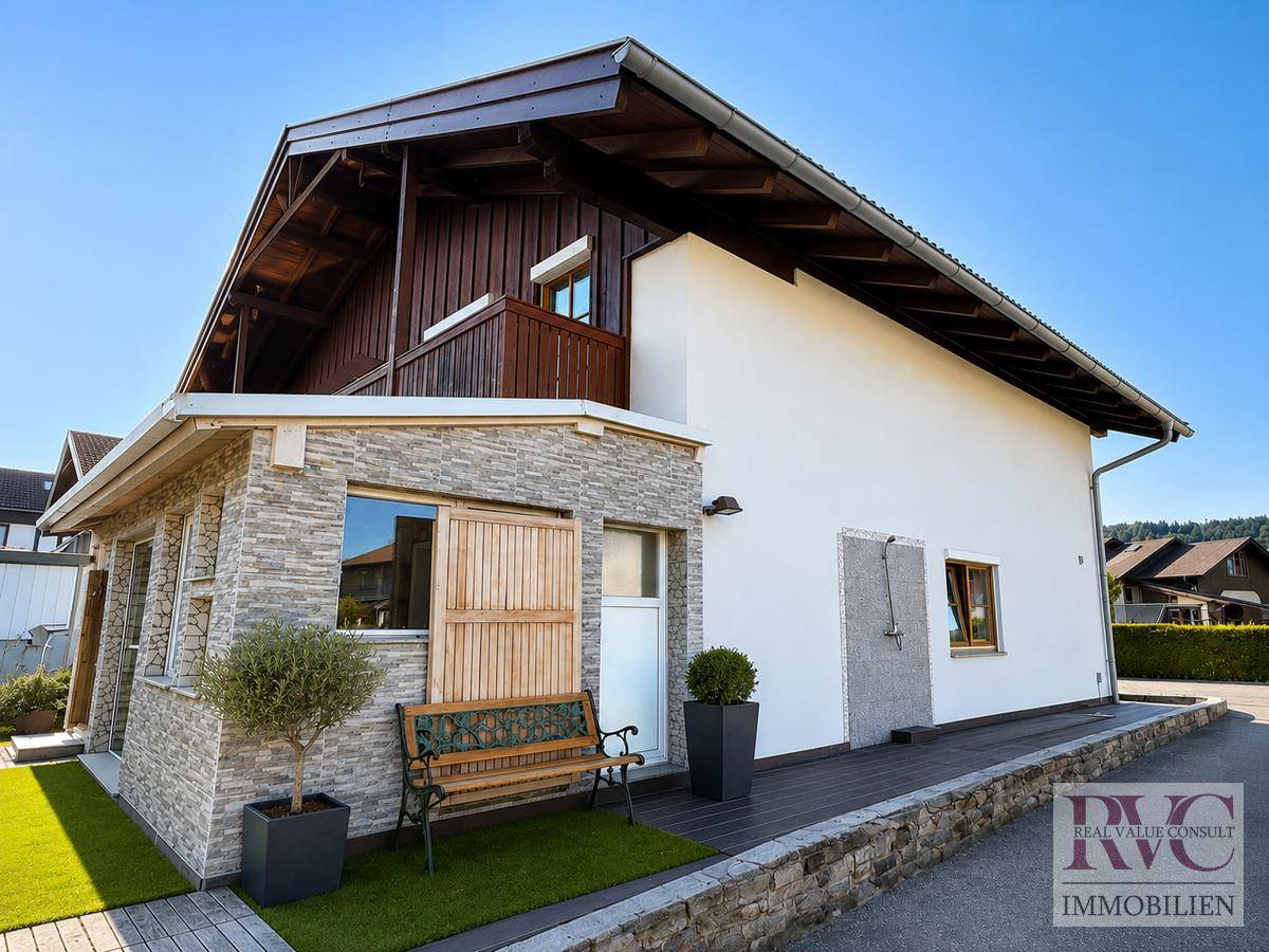 Seitenansicht des Hauses mit Holzbalkon, Steinverkleidung und einer Holzbank.