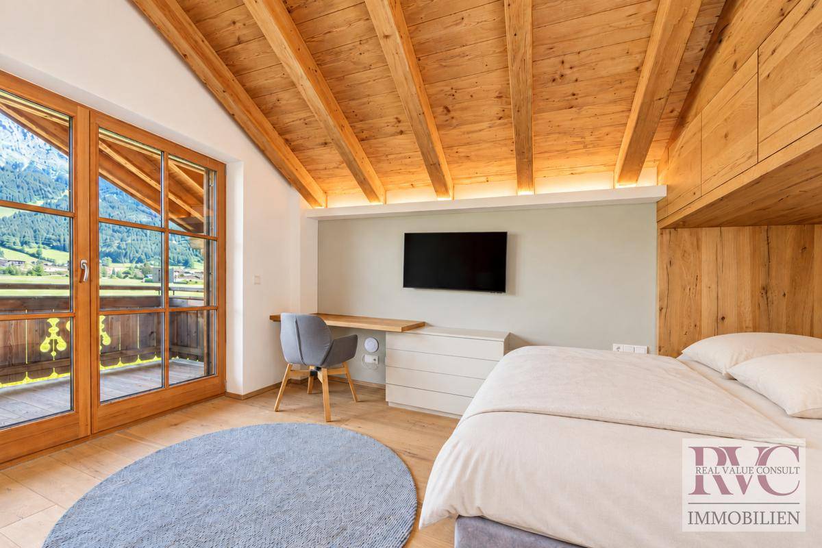 Gemütliches Schlafzimmer im Dachgeschoss mit Holzbalkendecke und Balkonzugang.