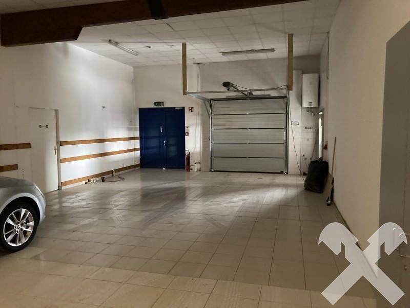 Geräumige Werkstatt oder Lagerhalle mit Rolltor, Fliesenboden und Zugangstüren, bereit für den Betrieb.