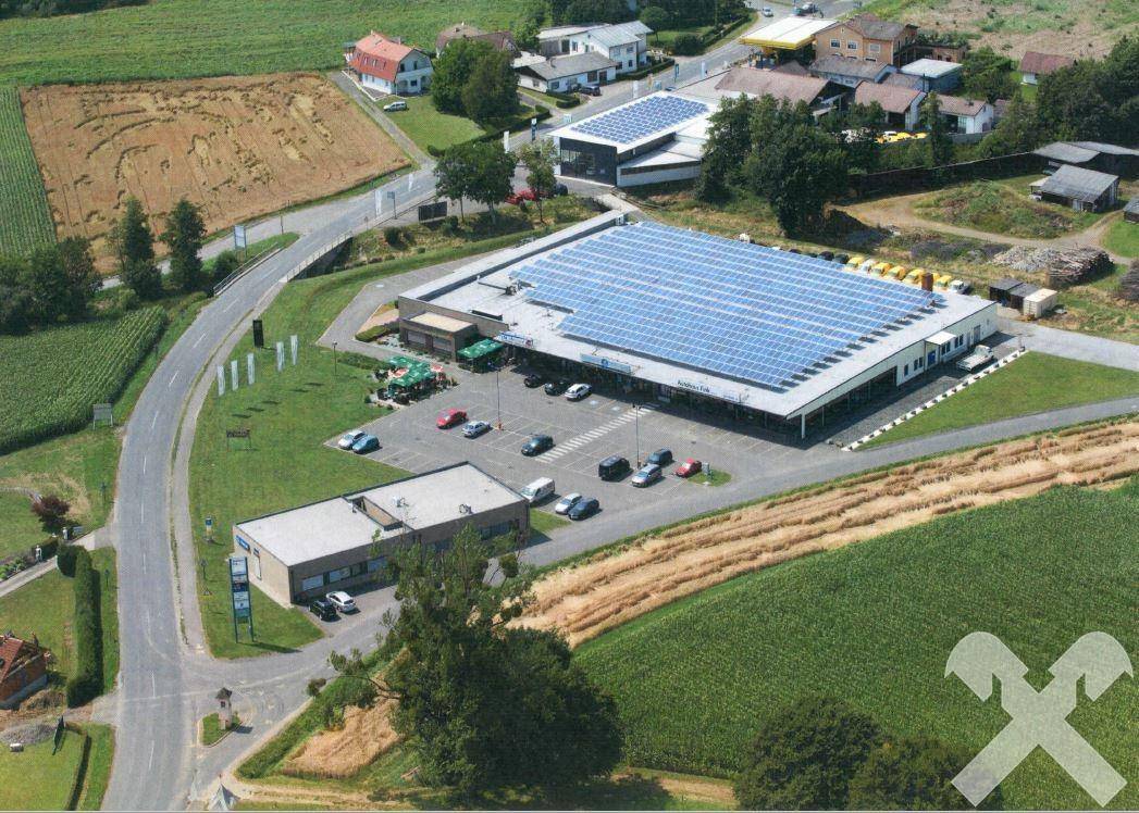 Luftaufnahme des Gewerbeobjekts mit Photovoltaikanlage auf dem Dach und umliegender grüner Landschaft.