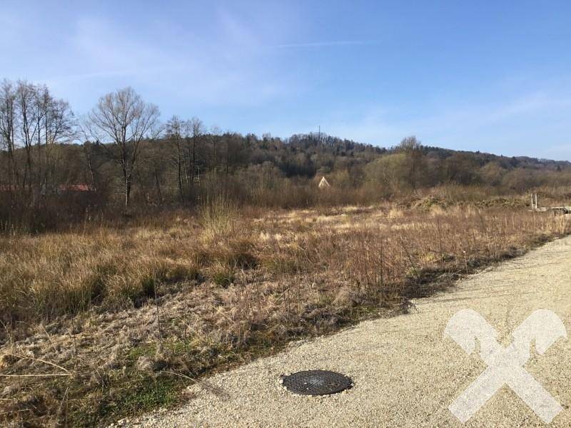 Weitläufiges Grundstück mit Schotterweg und Blick auf die bewaldete Hügellandschaft unter klarem Himmel.