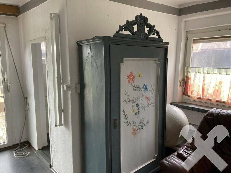 Schlafzimmer mit einem antiken, bemalten Kleiderschrank und einem Fenster mit Blick nach draußen.