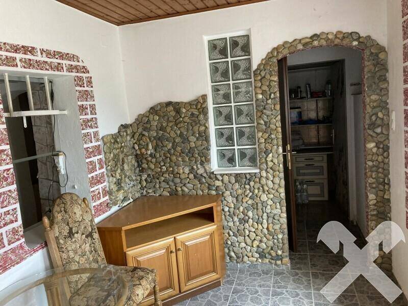 Heller Raum mit Steinwänden, Glasbausteinfenster und einem Holztisch mit Stühlen.