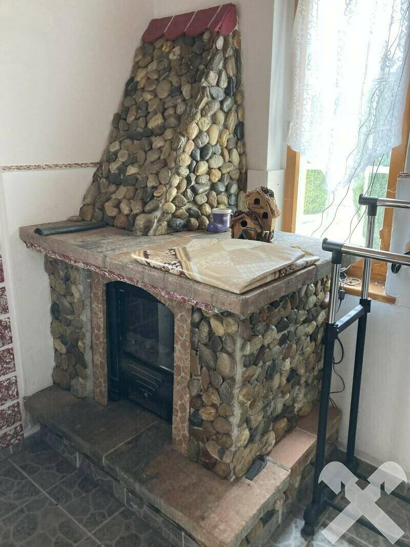 Rustikaler Kamin aus Flusssteinen mit einem Holzofen und einem Fenster mit Vorhängen.
