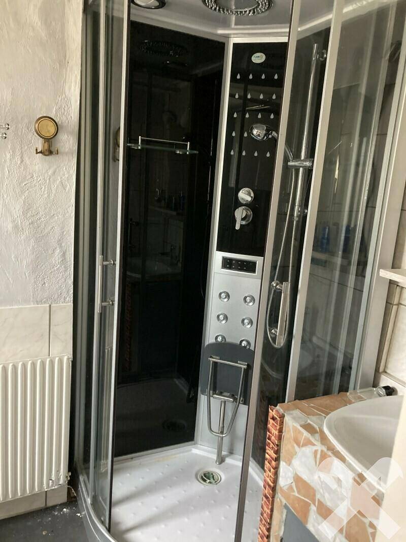 Modernisierte Dusche mit Glaswänden und Massagedüsen in einem gefliesten Badezimmer.