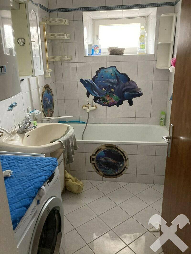 Badezimmer mit Badewanne, Waschbecken und Fliesenboden, dekoriert mit maritimen Motiven.