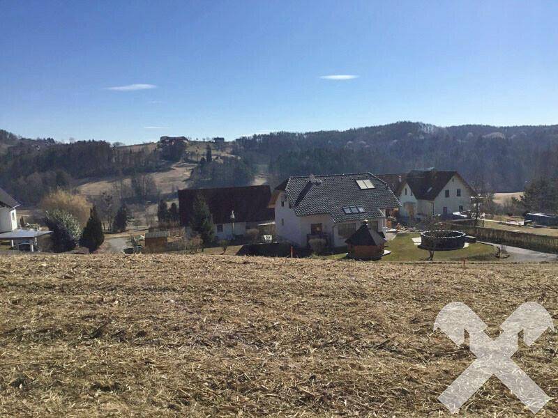 Panoramablick über eine ländliche Siedlung mit mehreren Häusern und weiten Hügeln unter blauem Himmel.