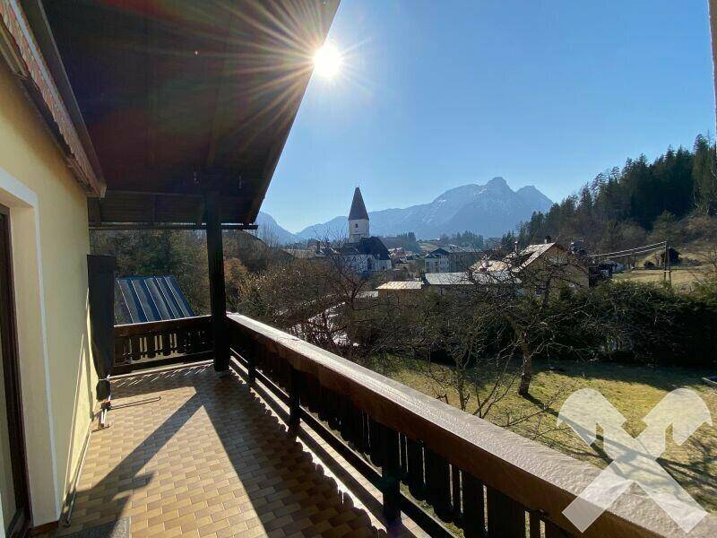 Sonniger Balkon mit Holzboden und weitem Blick über die Stadt und die Berge.