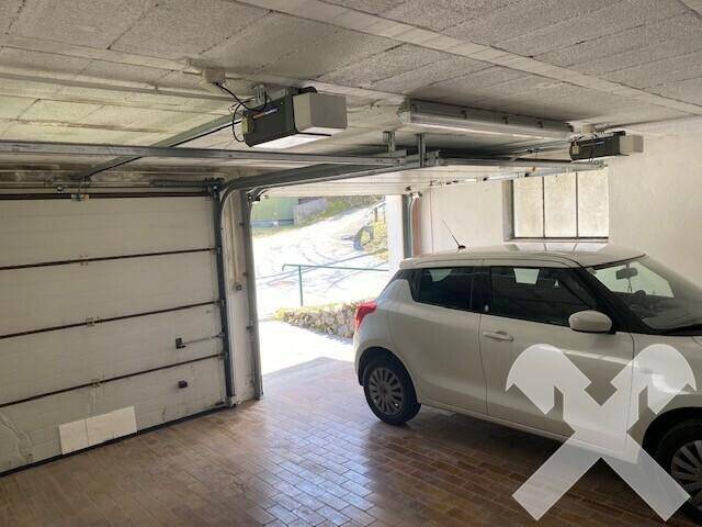 Innenansicht einer Garage mit einem geparkten Auto und automatischem Garagentor.