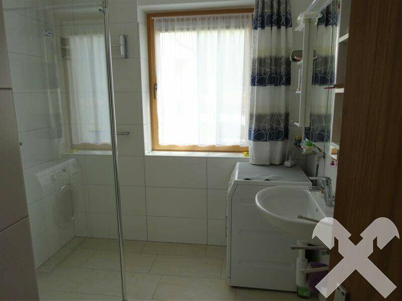 Helles Badezimmer mit Dusche, Waschmaschine und Fenster.