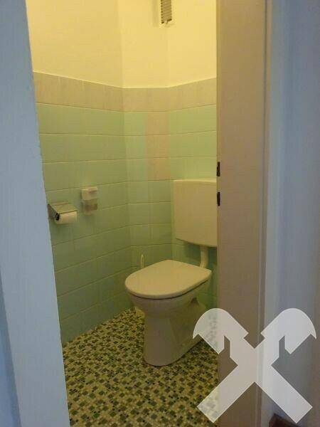 Separate Toilette mit hellgrünen Fliesen und gemustertem Boden.