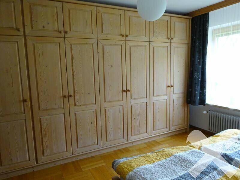 Schlafzimmer mit großen Holzschränken, Parkettboden und Fenster.