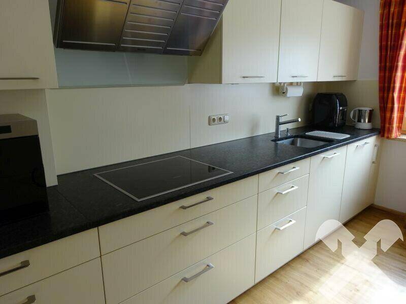 Moderne Küche mit dunkler Arbeitsplatte, Induktionskochfeld und Dunstabzugshaube.