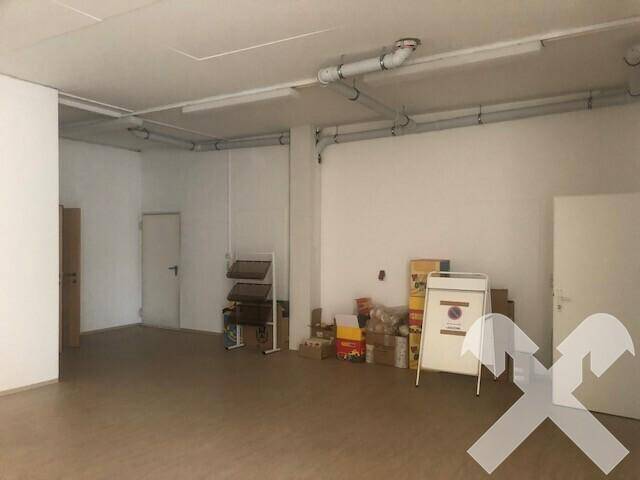 Geräumiger Lagerraum mit sichtbaren Rohren an der Decke, Leuchtstofflampen und verschiedenen Kartons.