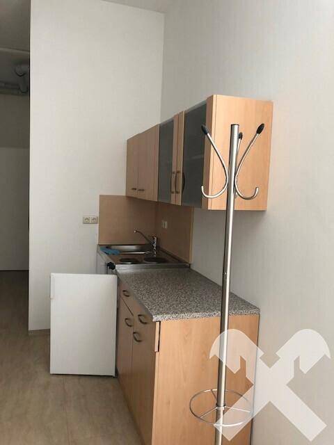 Kleine Küchenzeile mit Holzschränken, Granit-Arbeitsplatte und einem Kühlschrank in einem hellen Raum.
