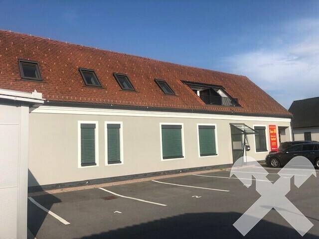 Seitenansicht des Gebäudes mit mehreren Fenstern, Rollläden und Dachfenstern, sowie einem Parkplatz davor.