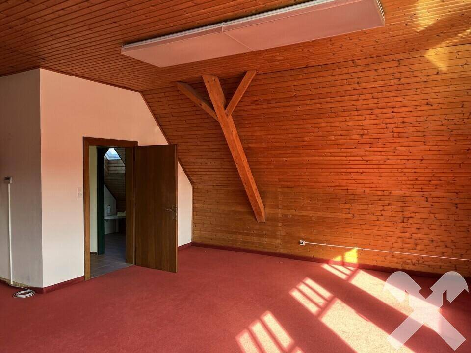 Blick in den Konferenzraum mit Holztüren, schrägen Wänden und sichtbaren Holzbalken unter dem Dach.