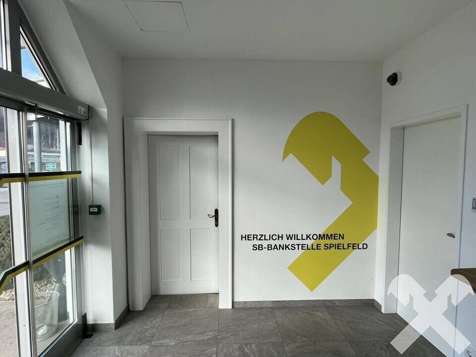 Heller Eingangsbereich mit modernen grauen Fliesen, weiß gestrichenen Wänden und einer großen Glastür.