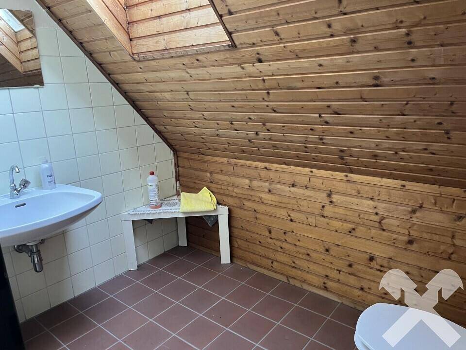 Kleines Badezimmer im Dachgeschoss mit Holzverkleidung, gefliestem Bereich, Waschbecken und schräger Decke.