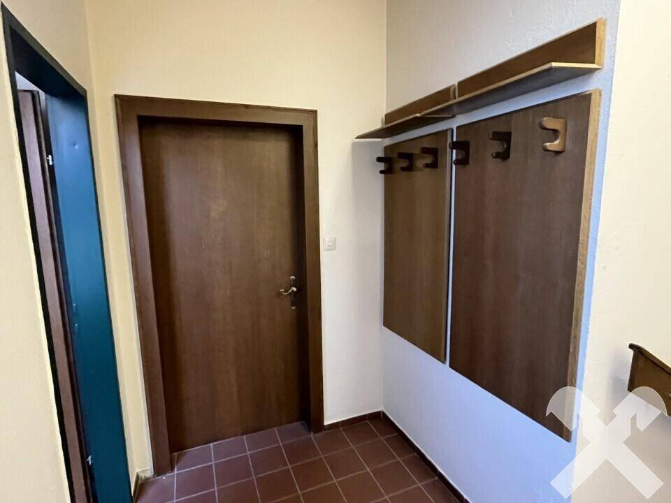 Eingangsbereich mit dunkler Holztür, Garderobe und Terrakotta-Fliesenboden.
