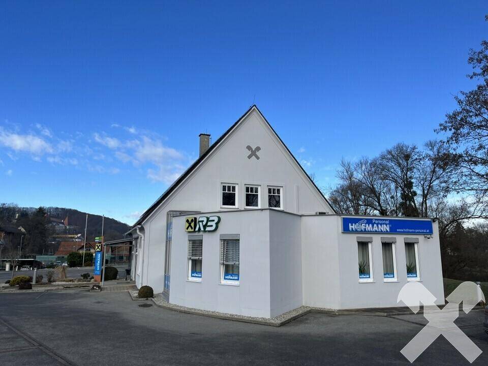 Außenansicht eines Geschäftsgebäudes mit weißer Fassade, Giebeldach und blauen Werbeschildern unter klarem Himmel.