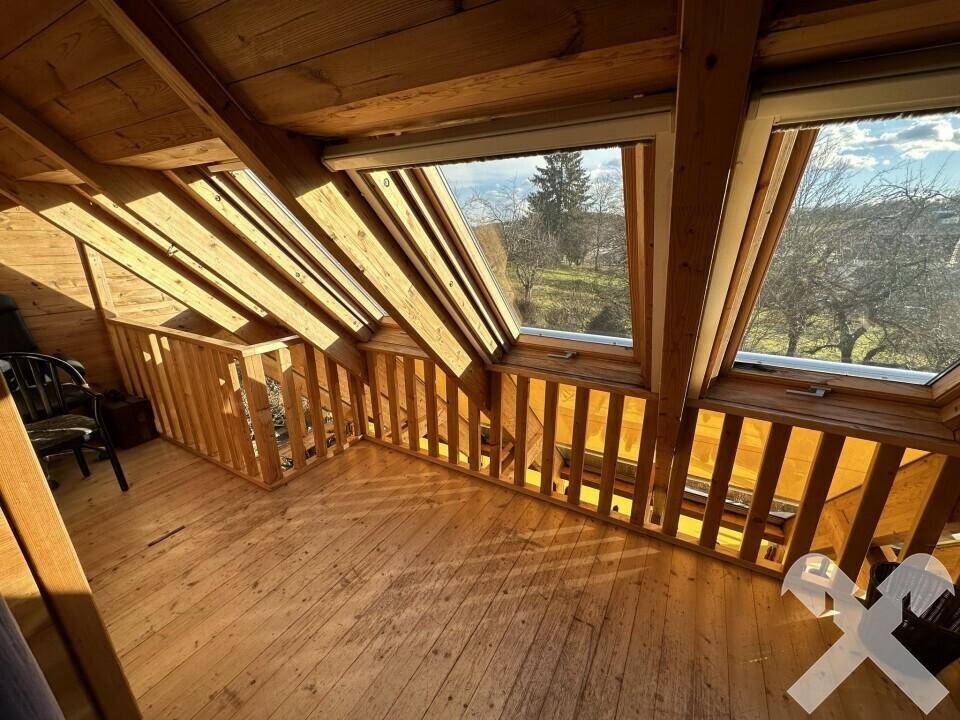 Heller Dachbodenbereich mit Holzboden, sichtbaren Balken und Dachfenstern mit Ausblick.