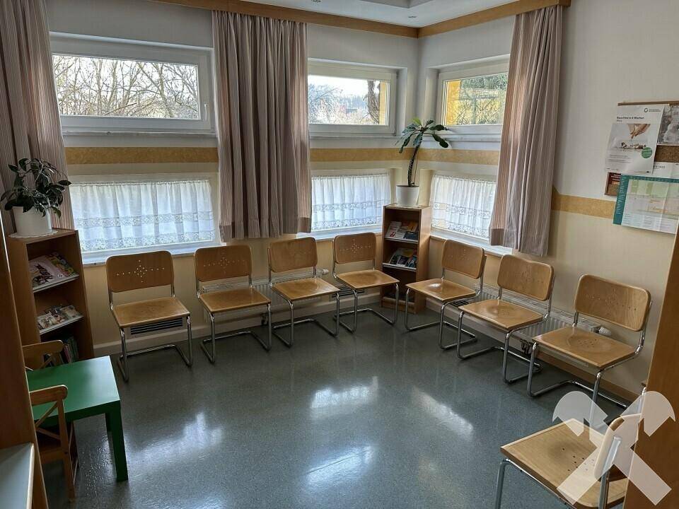 Wartezimmer mit mehreren Stühlen, großen Fenstern und natürlichem Lichteinfall.