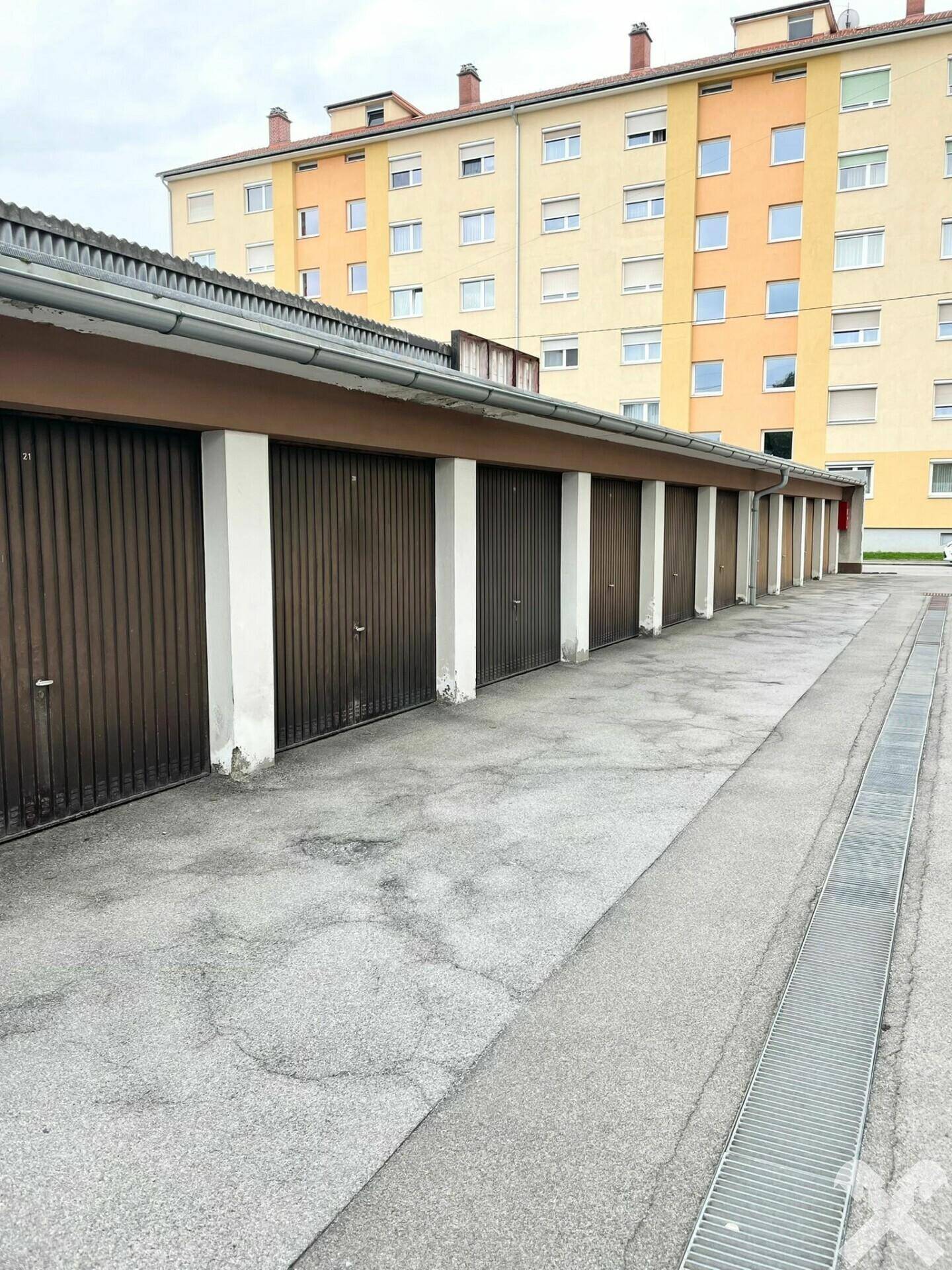 Reihe von Garagenboxen mit braunen Toren und einem Wohngebäude im Hintergrund.