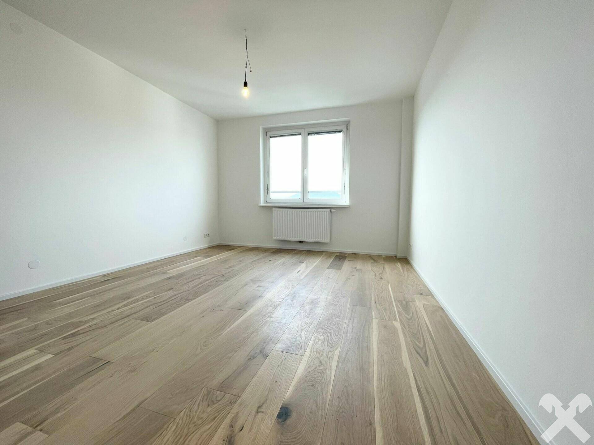 Leeres Zimmer mit hellem Holzplankenboden, weißen Wänden und einem Fenster.