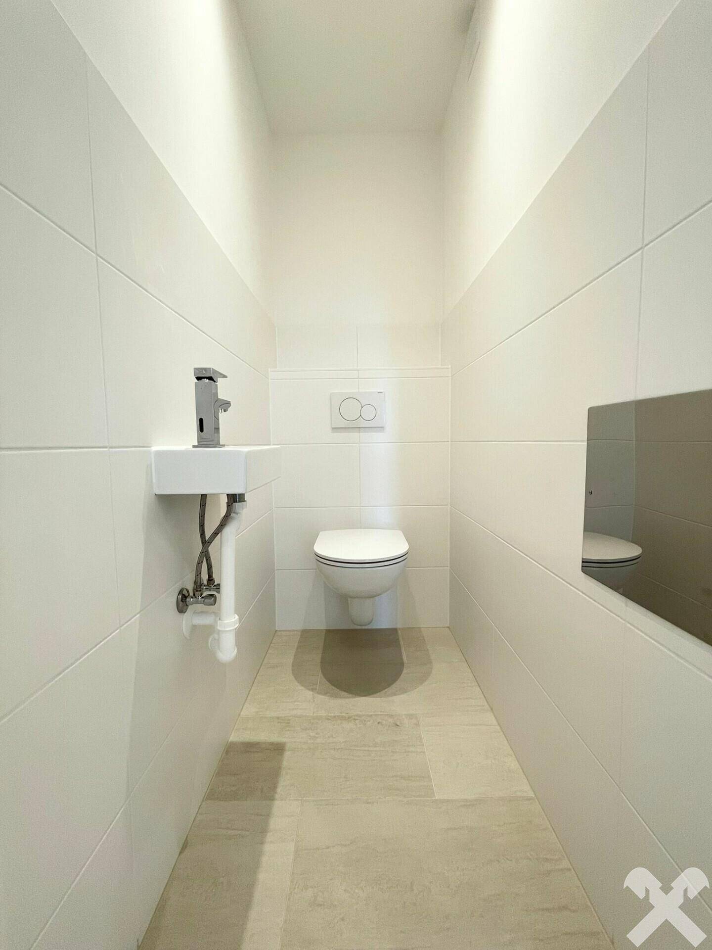Sauberer und heller WC-Raum mit wandhängender Toilette und kleinem Handwaschbecken.