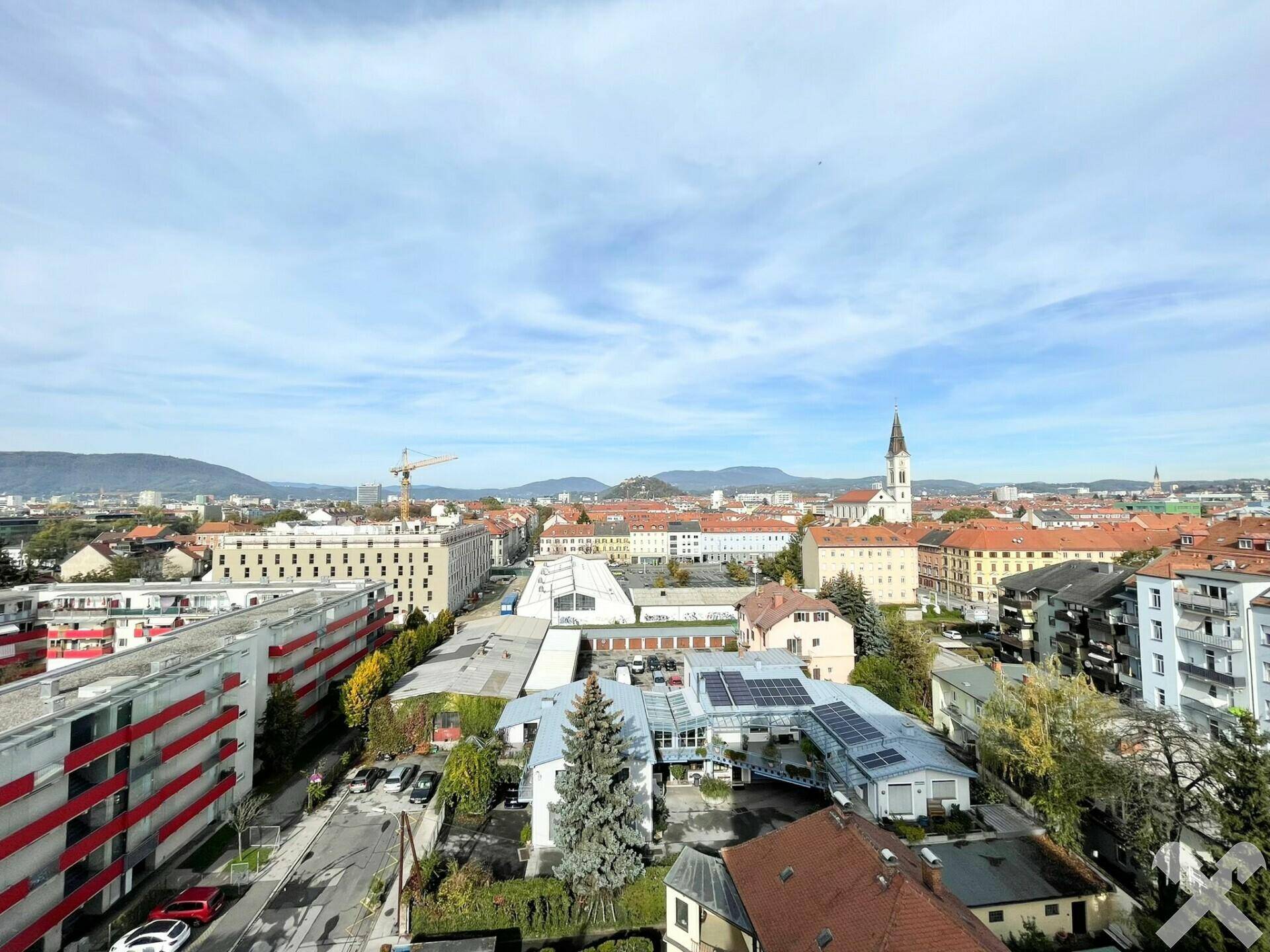 Weitläufiger Blick über die Stadt mit Wohngebäuden, Dächern und Bergen im Hintergrund.