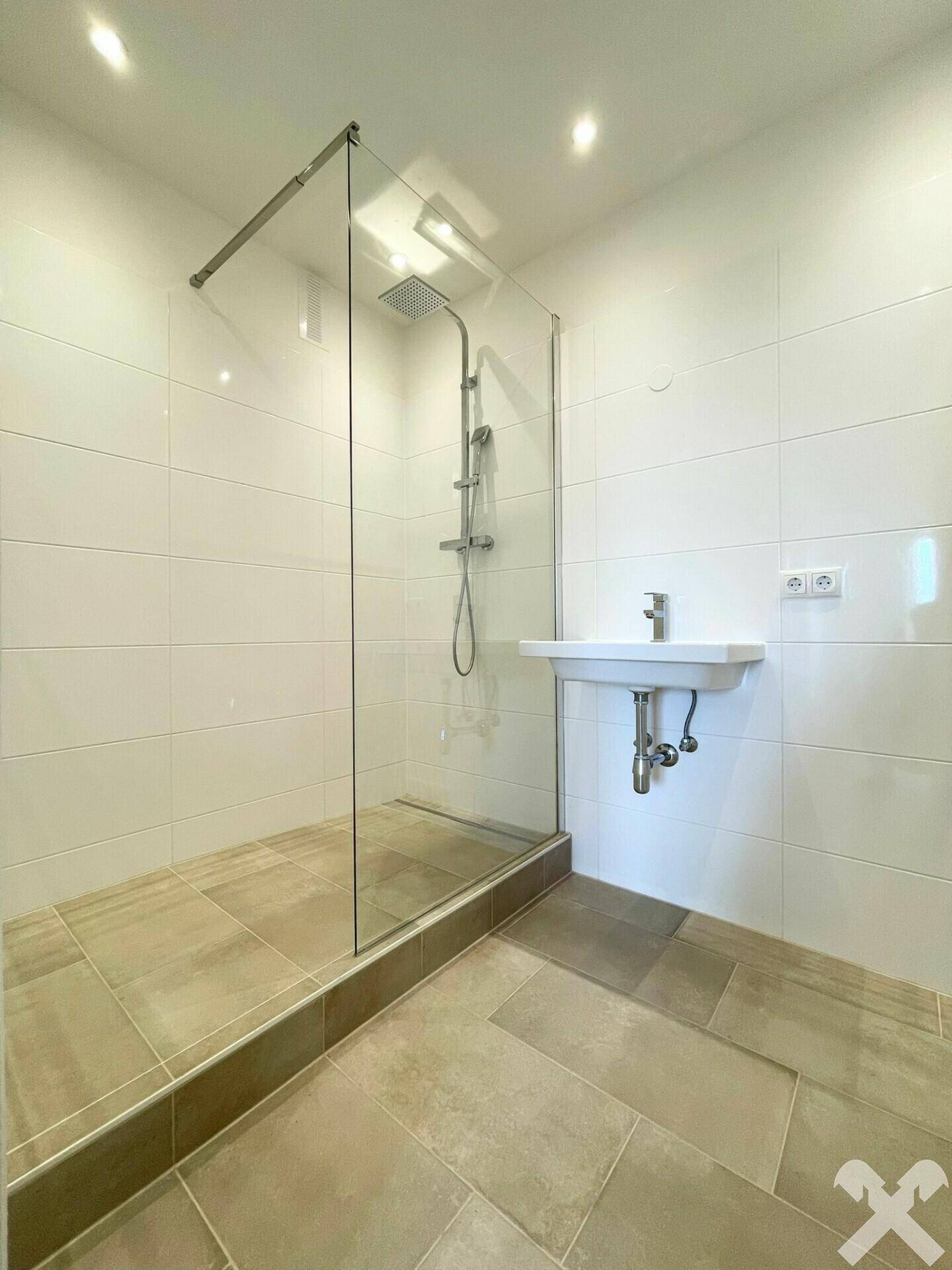 Modernes Badezimmer mit ebenerdiger Dusche, Glasabtrennung und Wandwaschbecken.