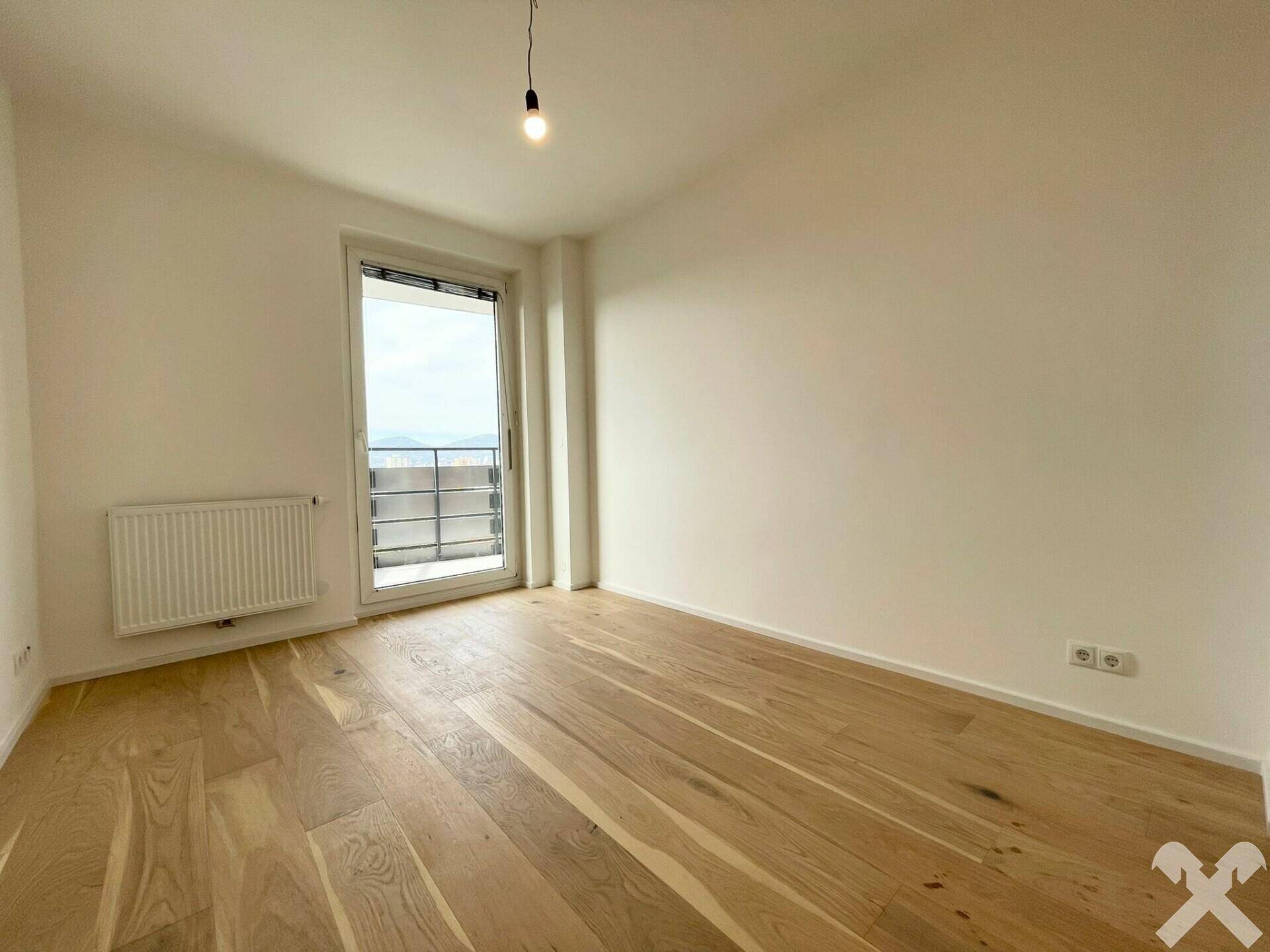 Helles Zimmer mit Zugang zu einem Balkon, ausgestattet mit Holzplankenboden und Heizkörper.