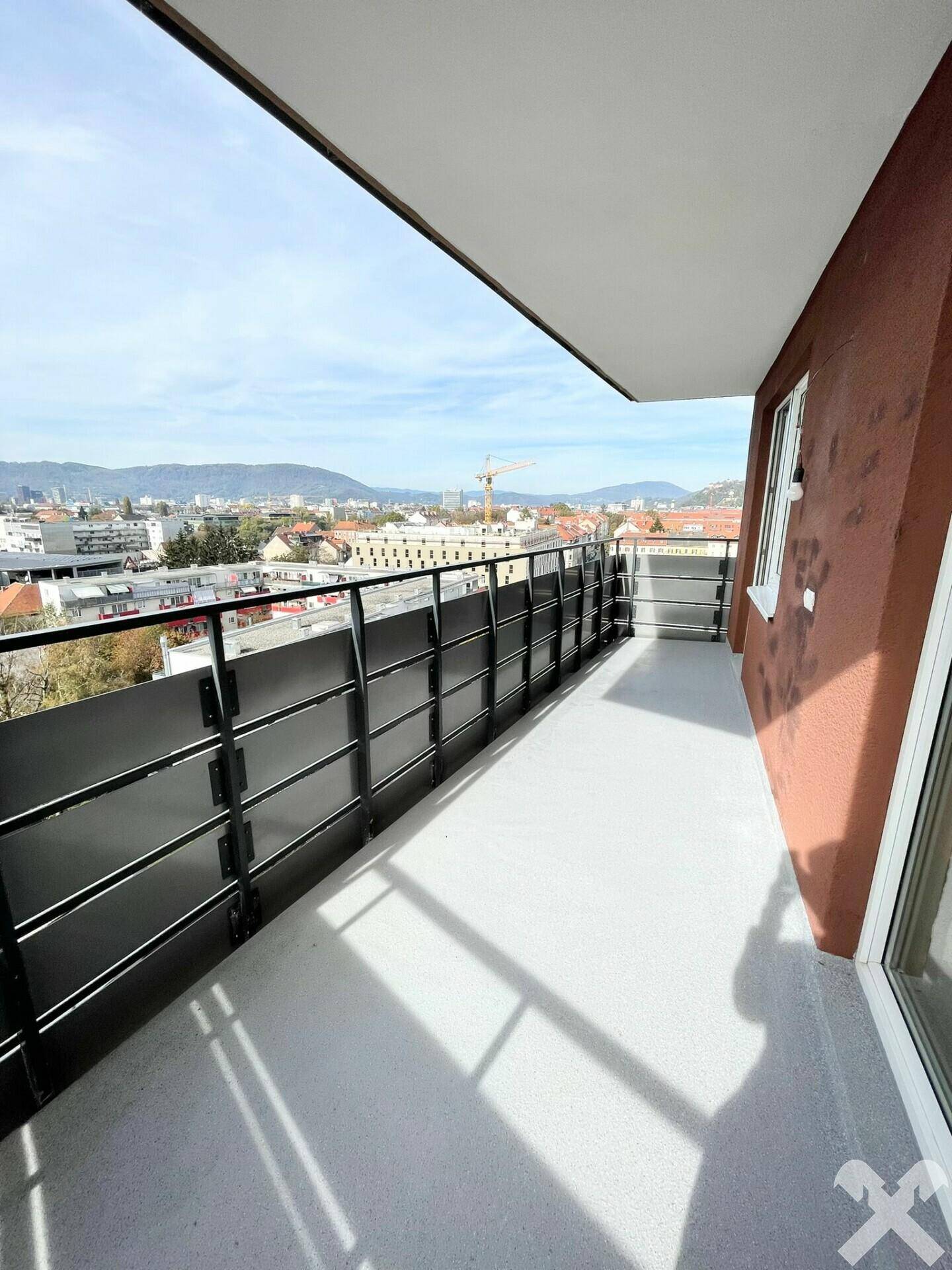 Geräumiger Balkon mit Blick auf die Stadt und die umliegenden Berge unter blauem Himmel.