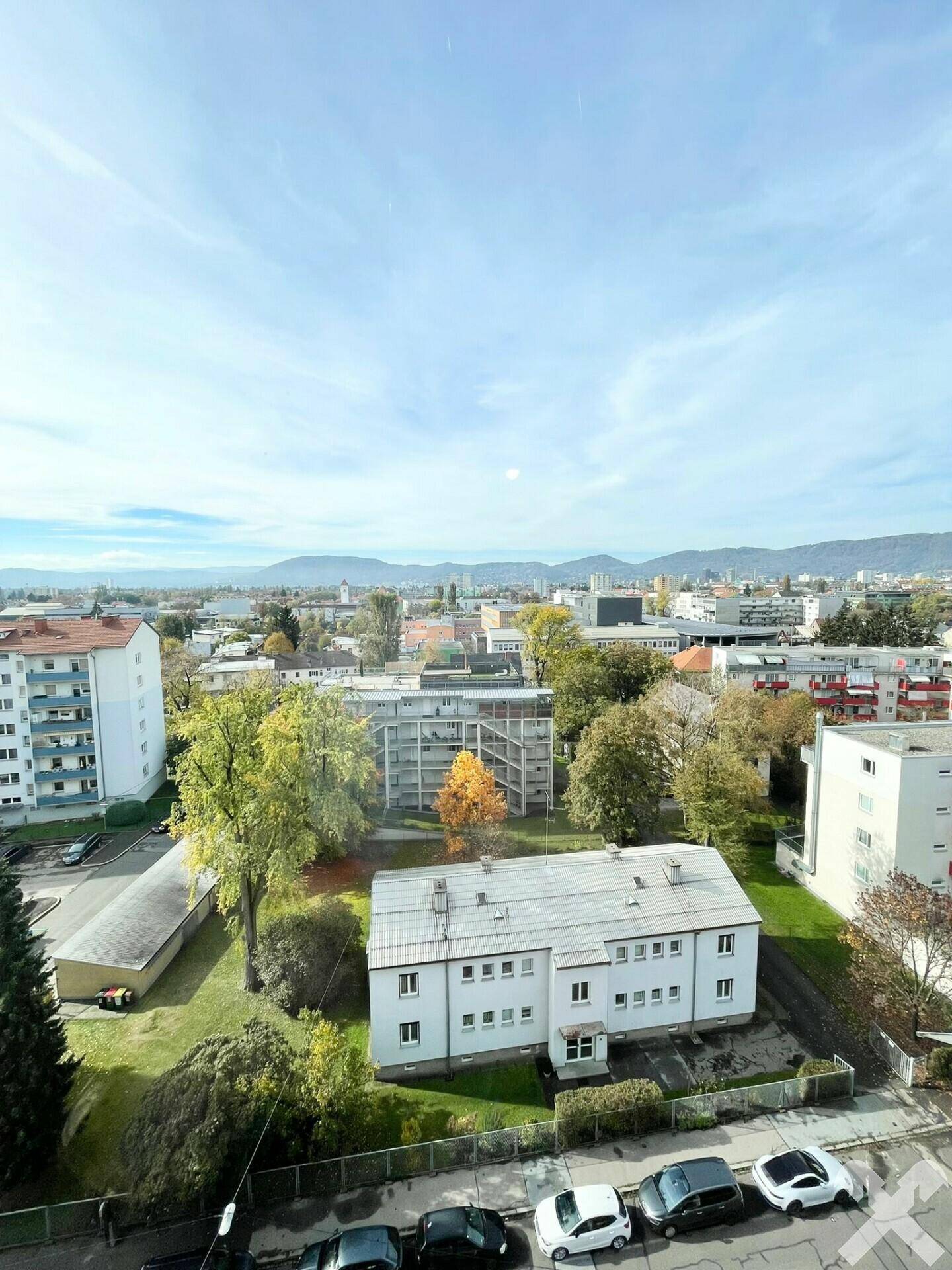 Ausblick auf Wohngebäude mit Grünflächen und Bäumen, umgeben von der städtischen Landschaft.