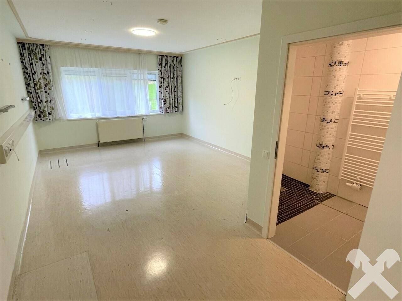 Geräumiges Zimmer mit großen Fenstern und Blick ins Grüne, angrenzend an ein Bad.