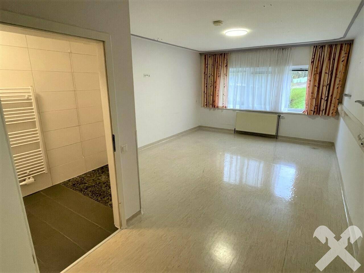 Helles Zimmer mit Fenster, Heizung und Zugang zu einem barrierefreien Badezimmer.