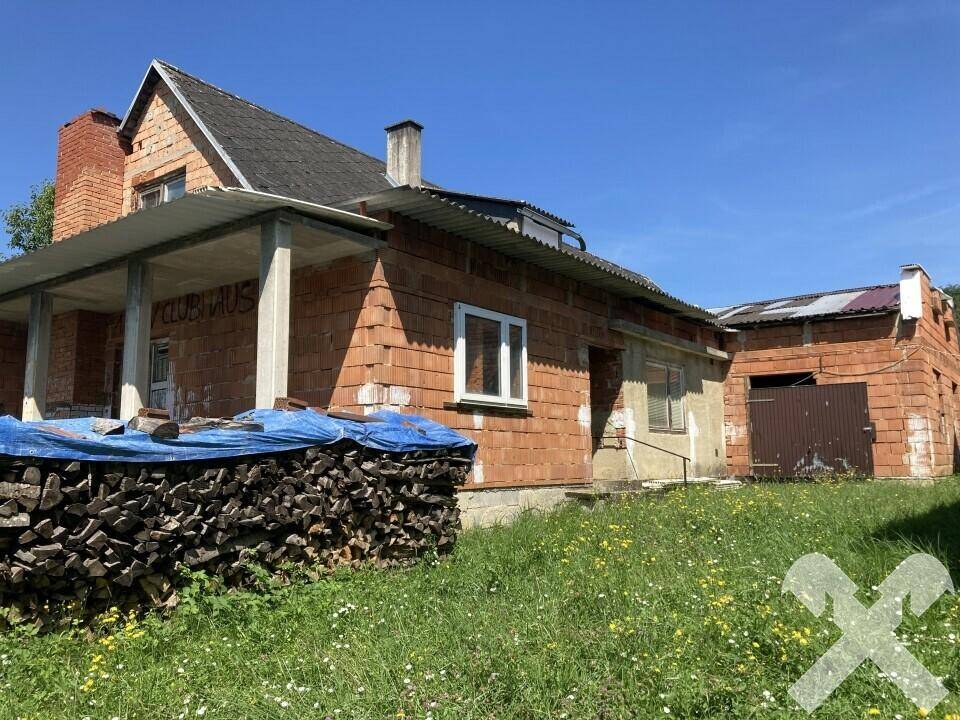 Nähere Ansicht des im Bau befindlichen Backsteingebäudes mit überdachtem Eingangsbereich und Holzstapeln.