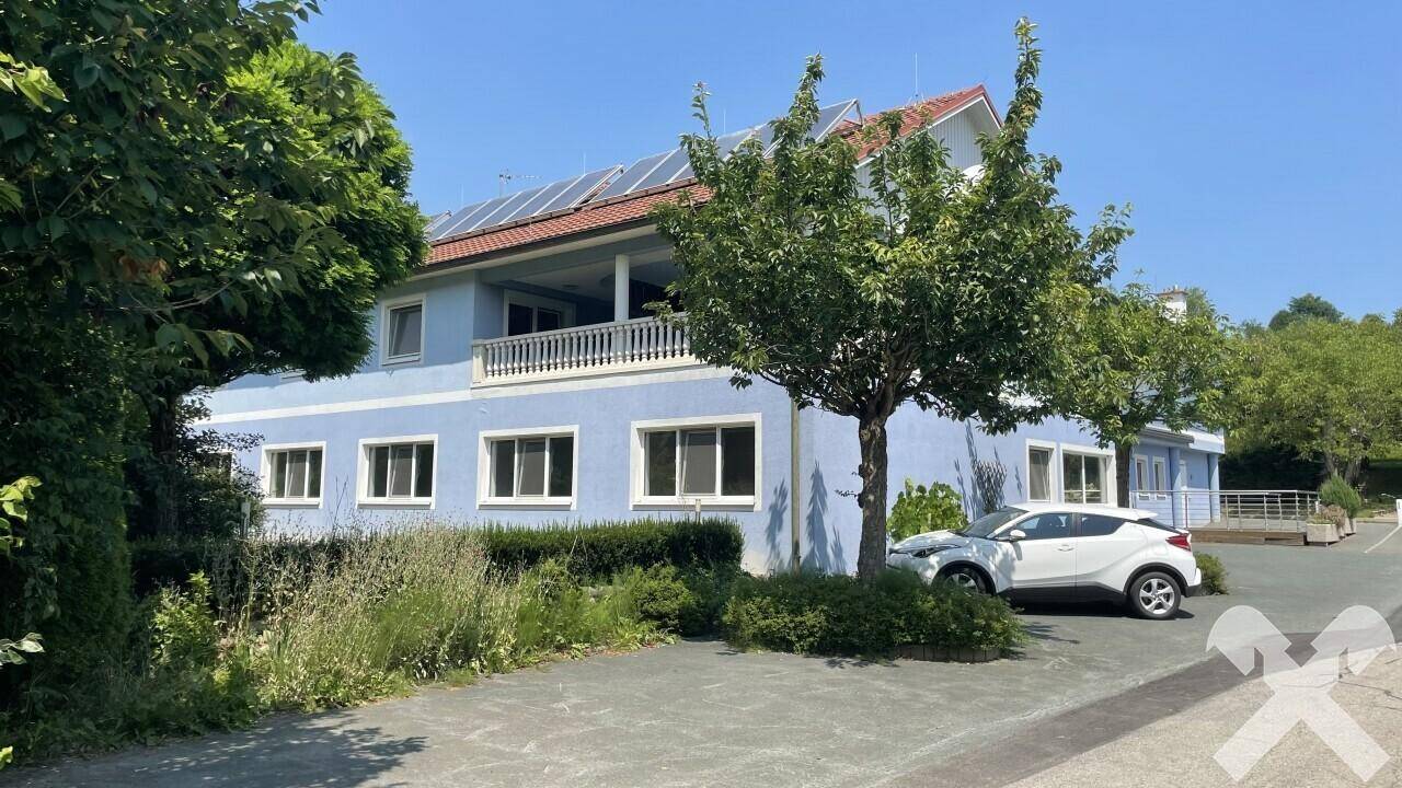 Blau gestrichenes Gebäude mit weißen Fenstern, Balkon und Solaranlage auf dem Dach an einem sonnigen Tag.